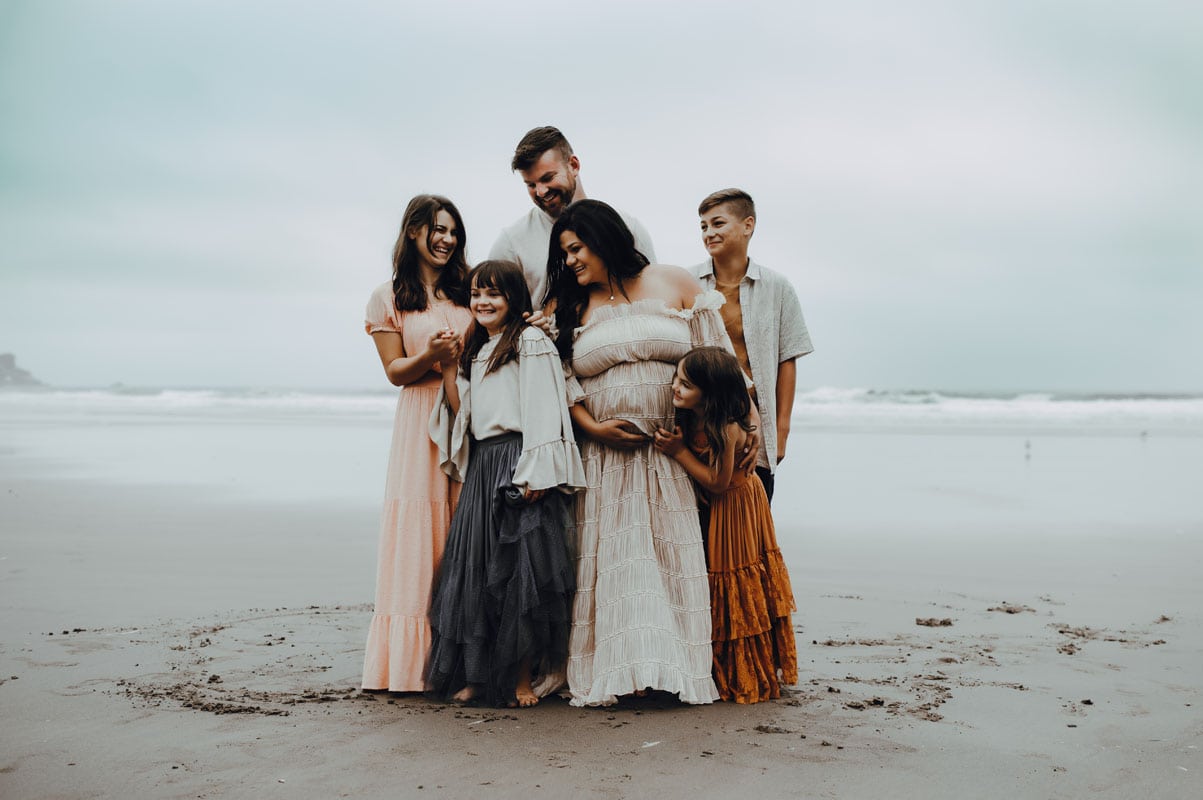 family of six stands at the beach posing during maternity session at oregon coast
