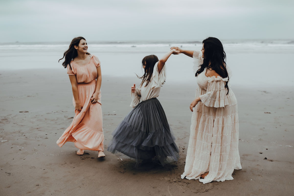 mom and two daughters dance by the beach