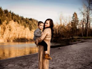 mom holds son and looks at him with pine trees in the background