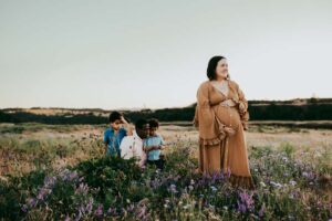 Pregnant woman in a field of wildflowers her husband and two sons behind her