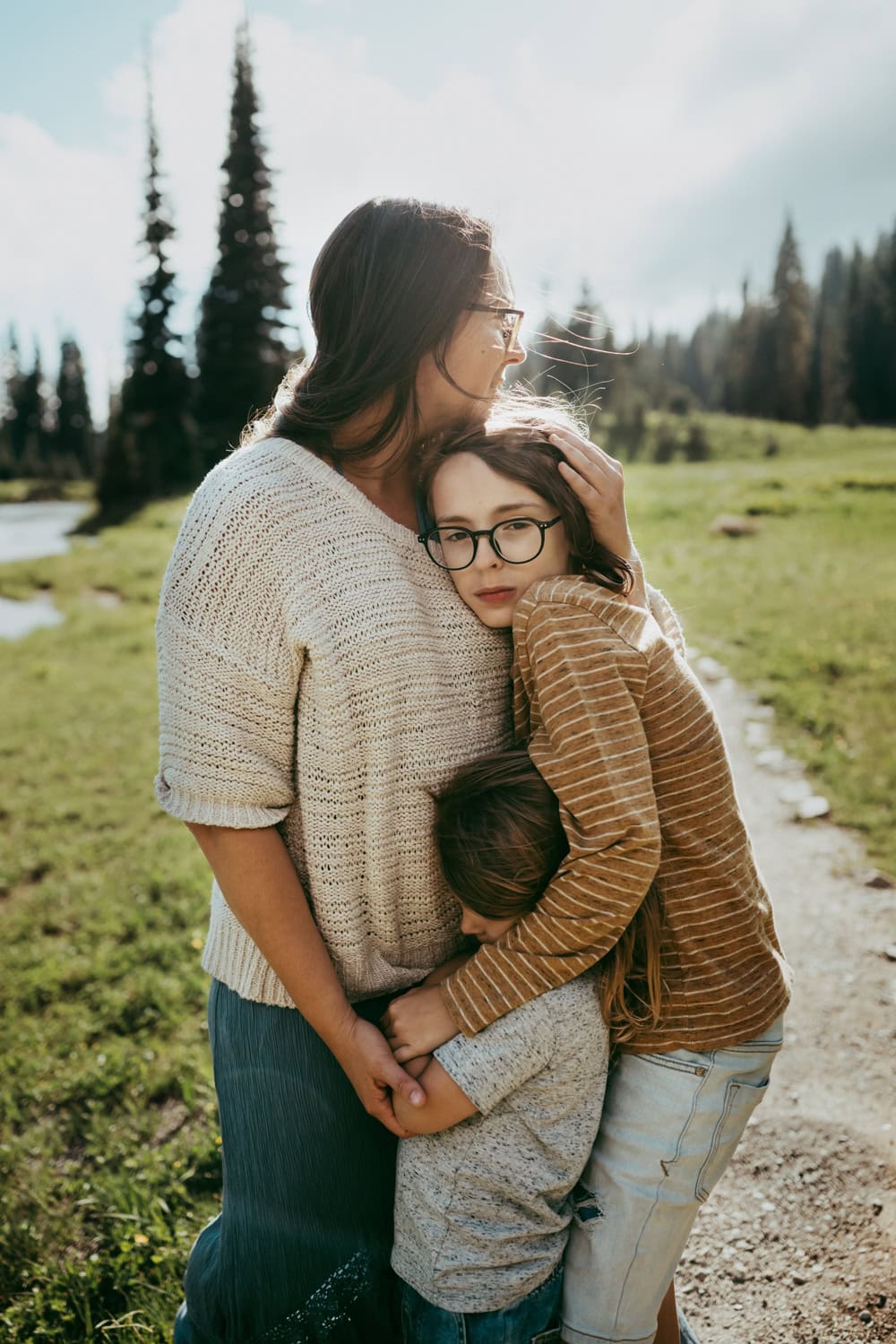 mother holds her children close with greenery in the background