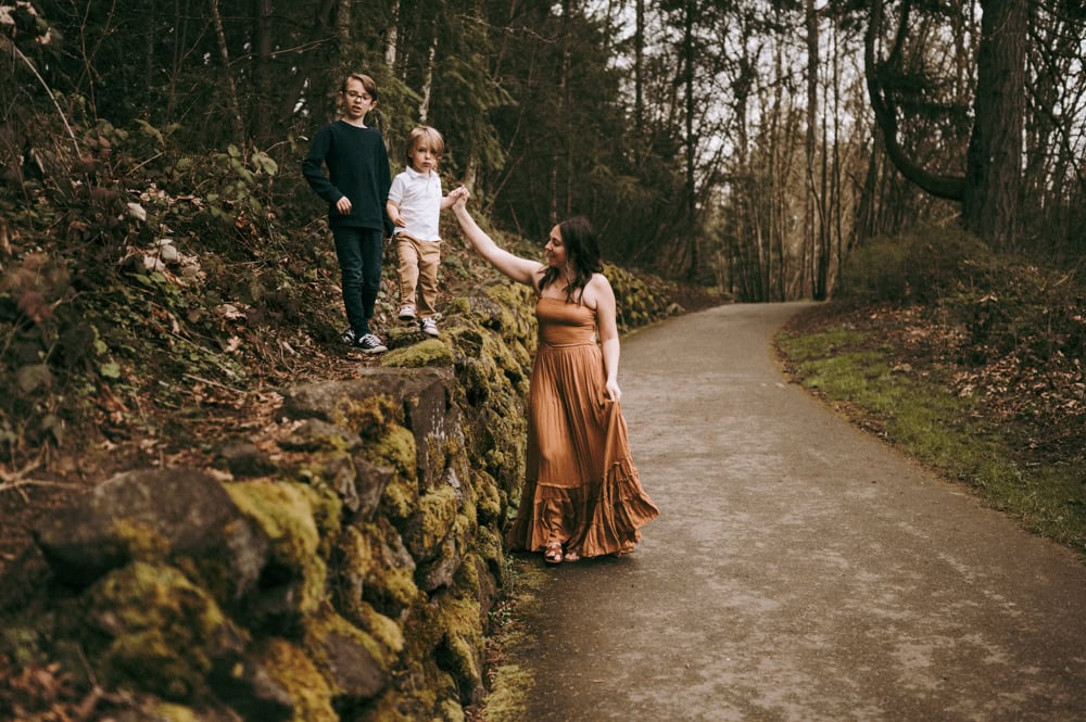 mother holds son's had while he walks on rocks